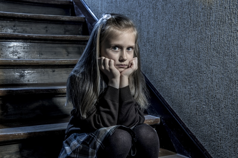 7 or 8 years old sad depressed and worried schoolgirl sitting on staircase desperate and scared suffering bullying and harassment at school