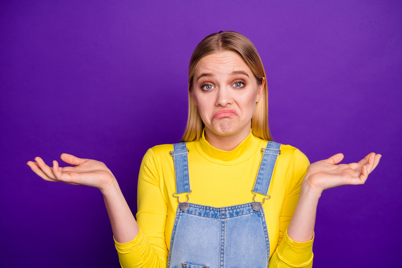Portrait of indifferent person shrugging her shoulders wearing yellow turtleneck denim jeans overalls isolated purple violet background