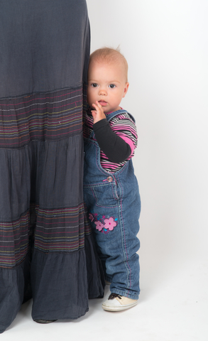 a little girl hiding behind her mother's skirt