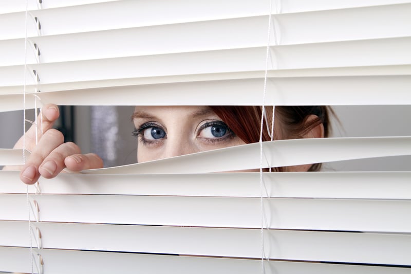 nosy woman peering through the window blinds