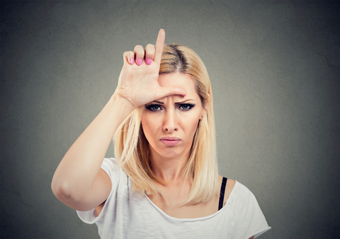 Closeup portrait unhappy woman giving loser sign on forehead, looking at you with anger and hatred on face isolated on gray background.